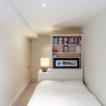 An open shelf at the end of a very narrow bedroom